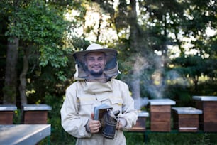 Portrait d’un apiculteur travaillant dans un rucher, tenant un fumoir d’abeille.
