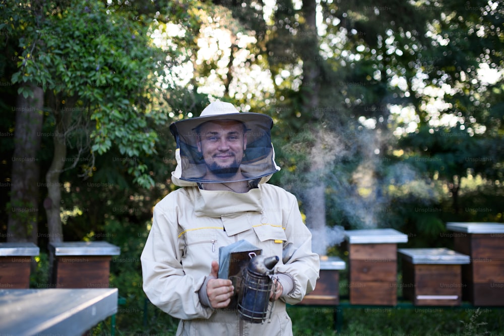 Un ritratto dell'apicoltore che lavora nell'apiario, tenendo in mano il fumatore di api.