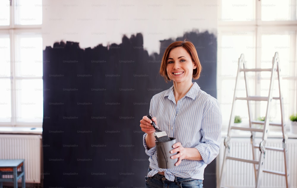 벽을 검은색으로 칠하는 젊은 창조적인 여성의 초상화. 중소기업의 창업.