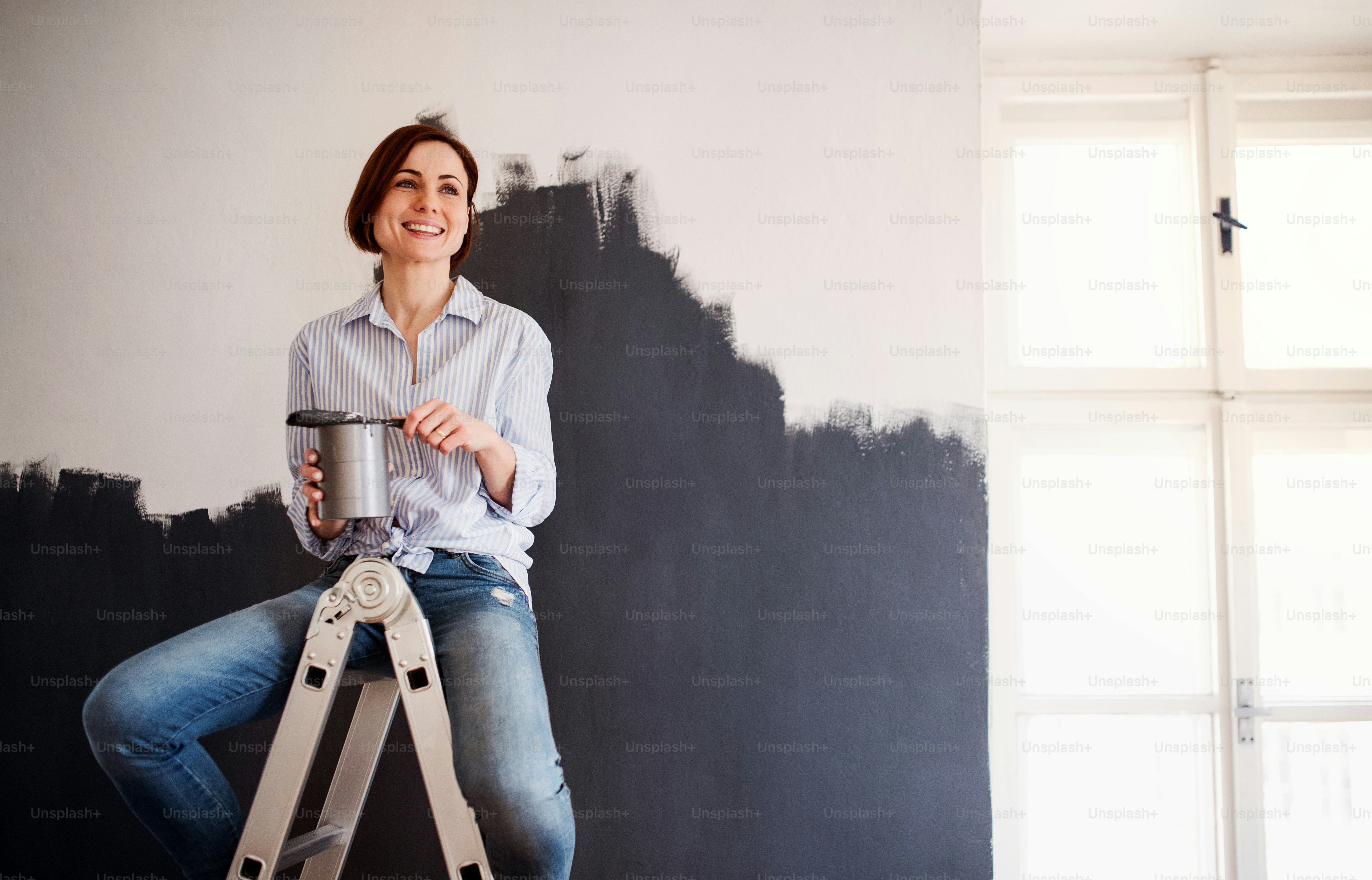 A portrait of young creative woman painting wall black. A startup of small business.
