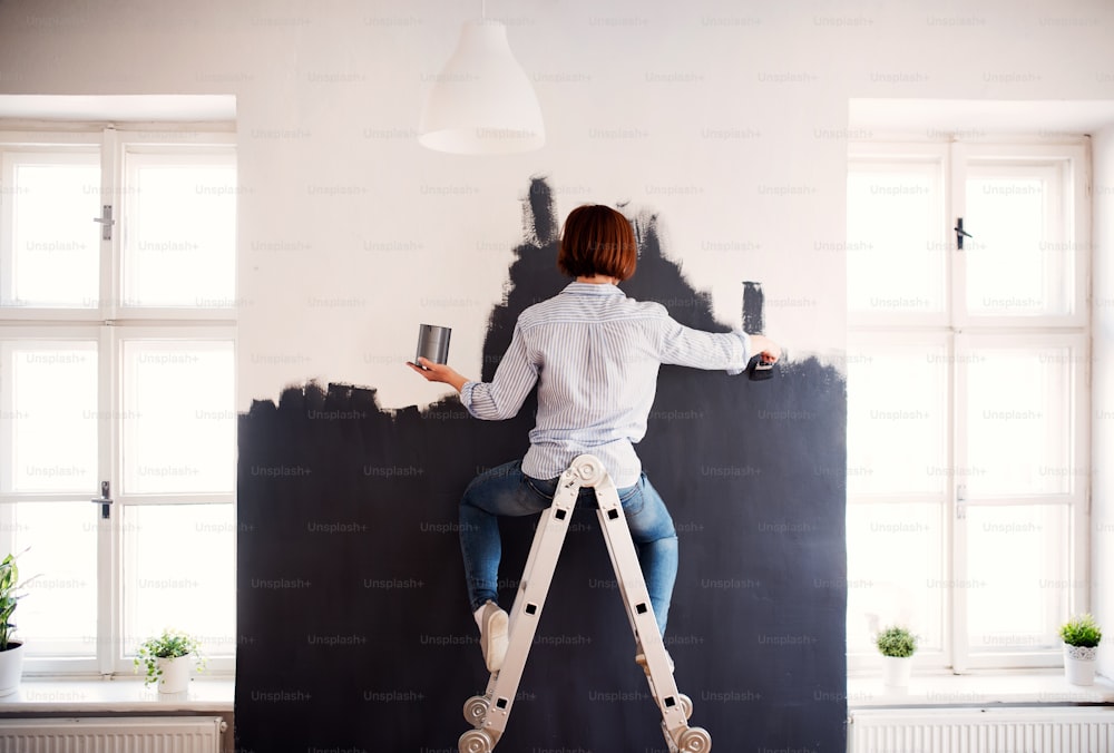 Una vista posteriore di giovane donna creativa che dipinge il muro di nero. Una startup di piccole imprese.