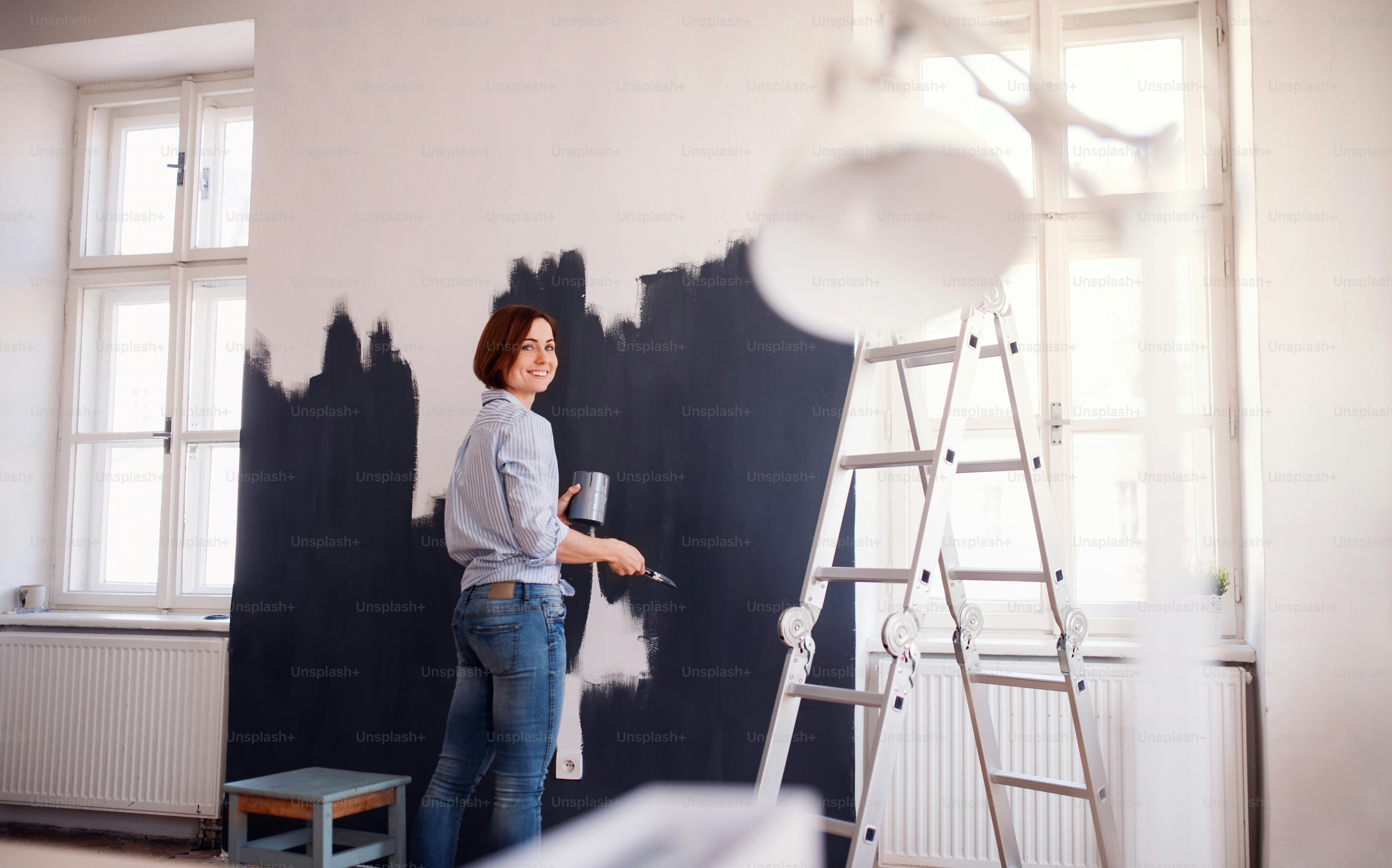A portrait of young creative woman painting wall black. A startup of small business