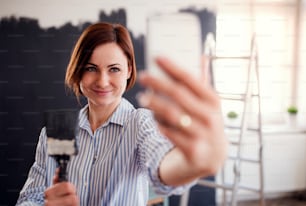Un retrato de una joven creativa con un teléfono inteligente pintando la pared de negro, tomándose una selfie. Una startup de pequeñas empresas.