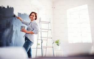 A portrait of young creative woman painting wall black. A startup of small business.