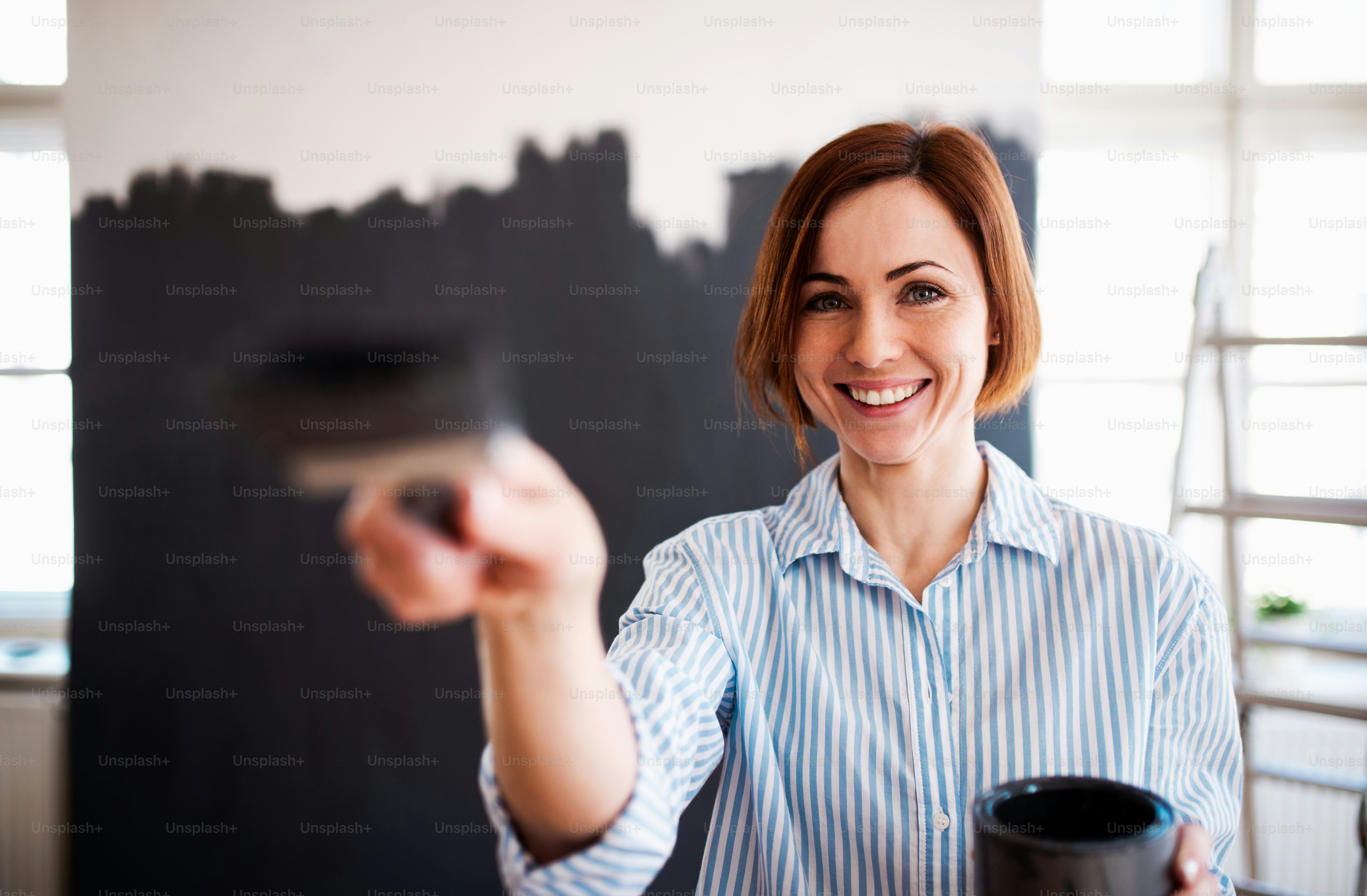 Ein Porträt einer jungen kreativen Frau, die die Wand schwarz streicht. Ein Startup eines kleinen Unternehmens.