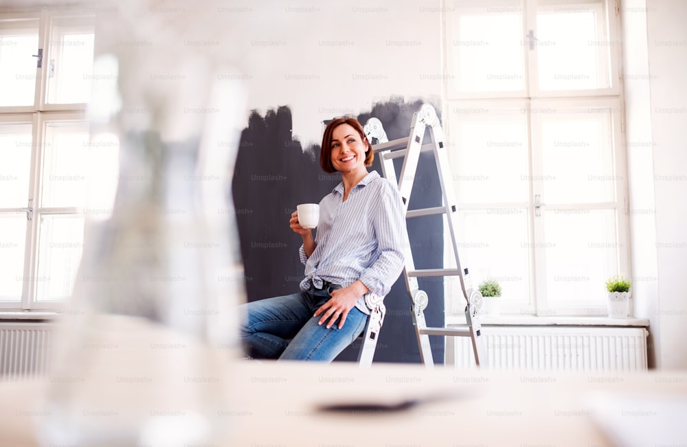 A portrait of young creative woman with a cup of coffee painting wall black. A startup of small business.