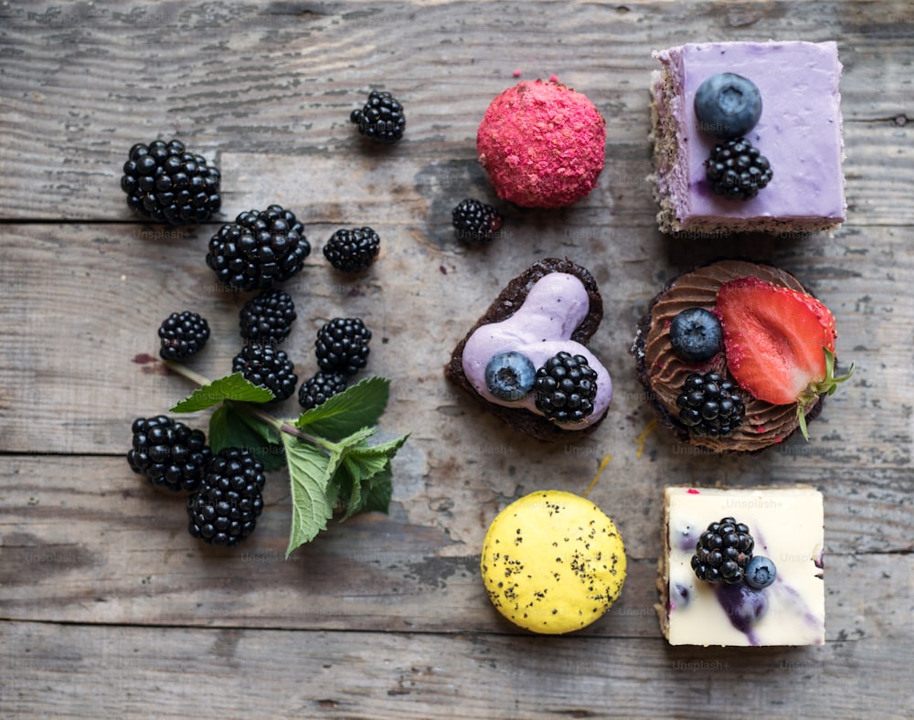 Vista superior da seleção de sobremesas de bolo coloridas e deliciosas e frutas vermelhas na mesa de madeira.