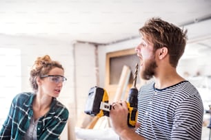Small business of a young couple. Man and woman worker with an electric drill in the carpenter workroom.