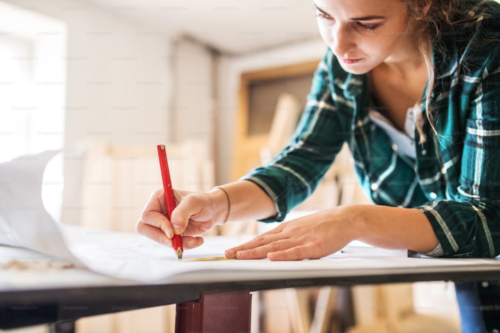 Kleines Geschäft einer jungen Frau. Schöne junge Arbeiterin im Arbeitszimmer. Schreinerin skizziert ein Projekt.