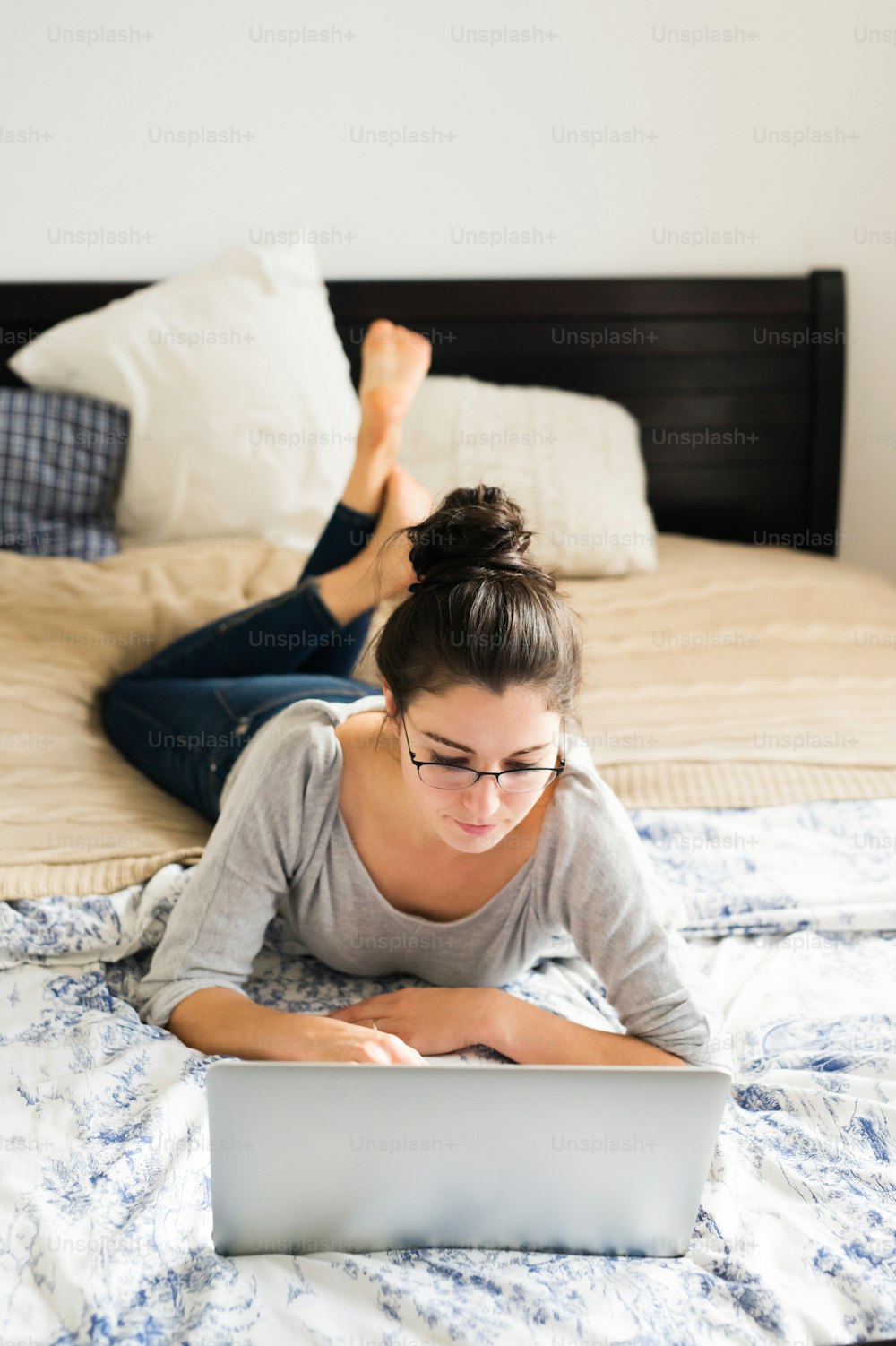 Beautiful young woman lying on bed, working on notebook, home office.