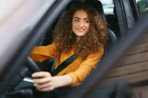 街で車を運転する若い女性。車の中で美しい女性のポートレート、窓の外を見て微笑む。