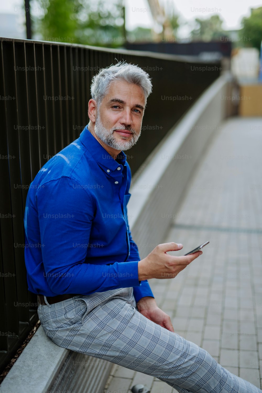Un exitoso hombre de negocios feliz esperando en la calle de la ciudad, usando el teléfono móvil, concepto de desplazamiento.