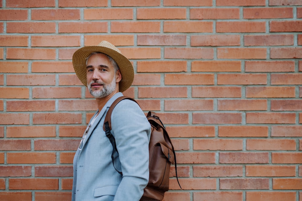 Ein Porträt eines selbstbewussten Mannes mit Strohhut und Rucksack, der in die Kamera schaut, Geschäftsmann in Freizeitkleidung im Sommer auf dem Weg zur Arbeit.