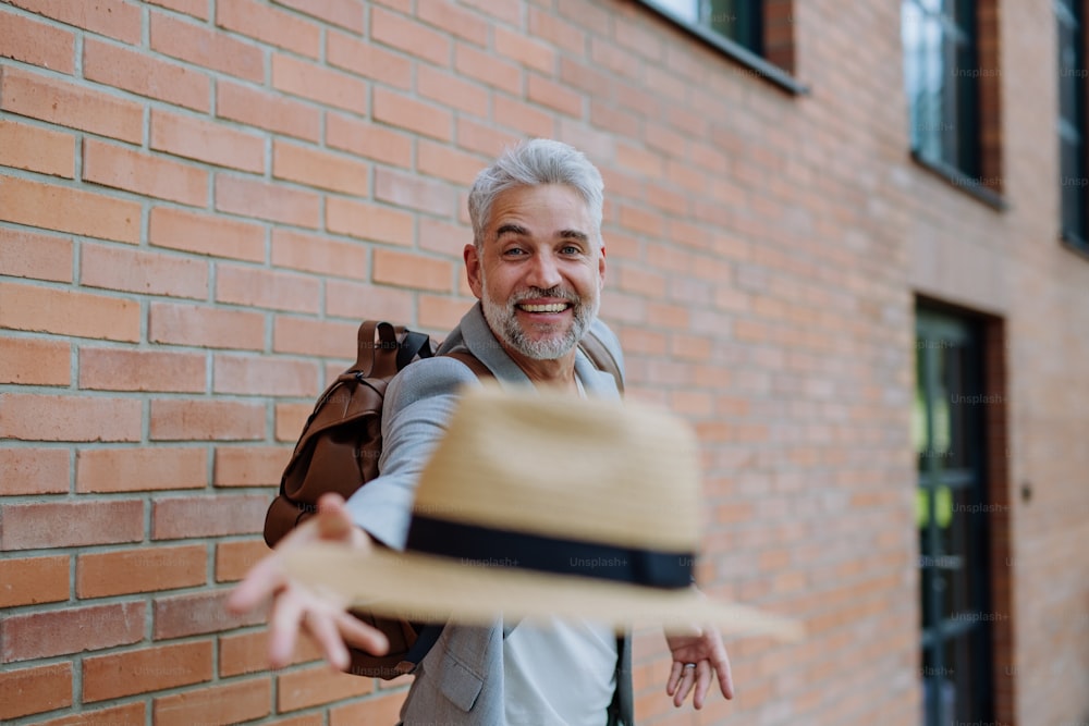麦わら帽子を投げてカメラを見る幸せな男性の面白いポートレート、夏に仕事に行く途中のカジュアルな服を着たビジネスマン。