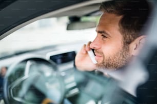 Gros plan d’un jeune homme d’affaires avec smartphone assis dans la voiture, faisant un appel téléphonique.