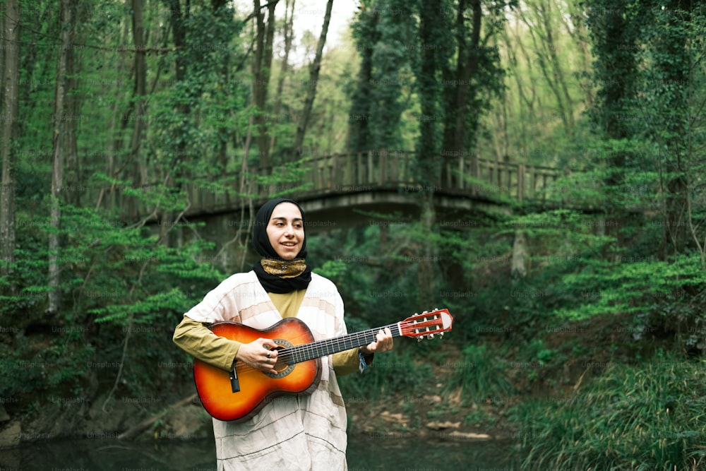 a woman standing in a forest holding a guitar