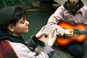 two people sitting on a dock playing a musical instrument