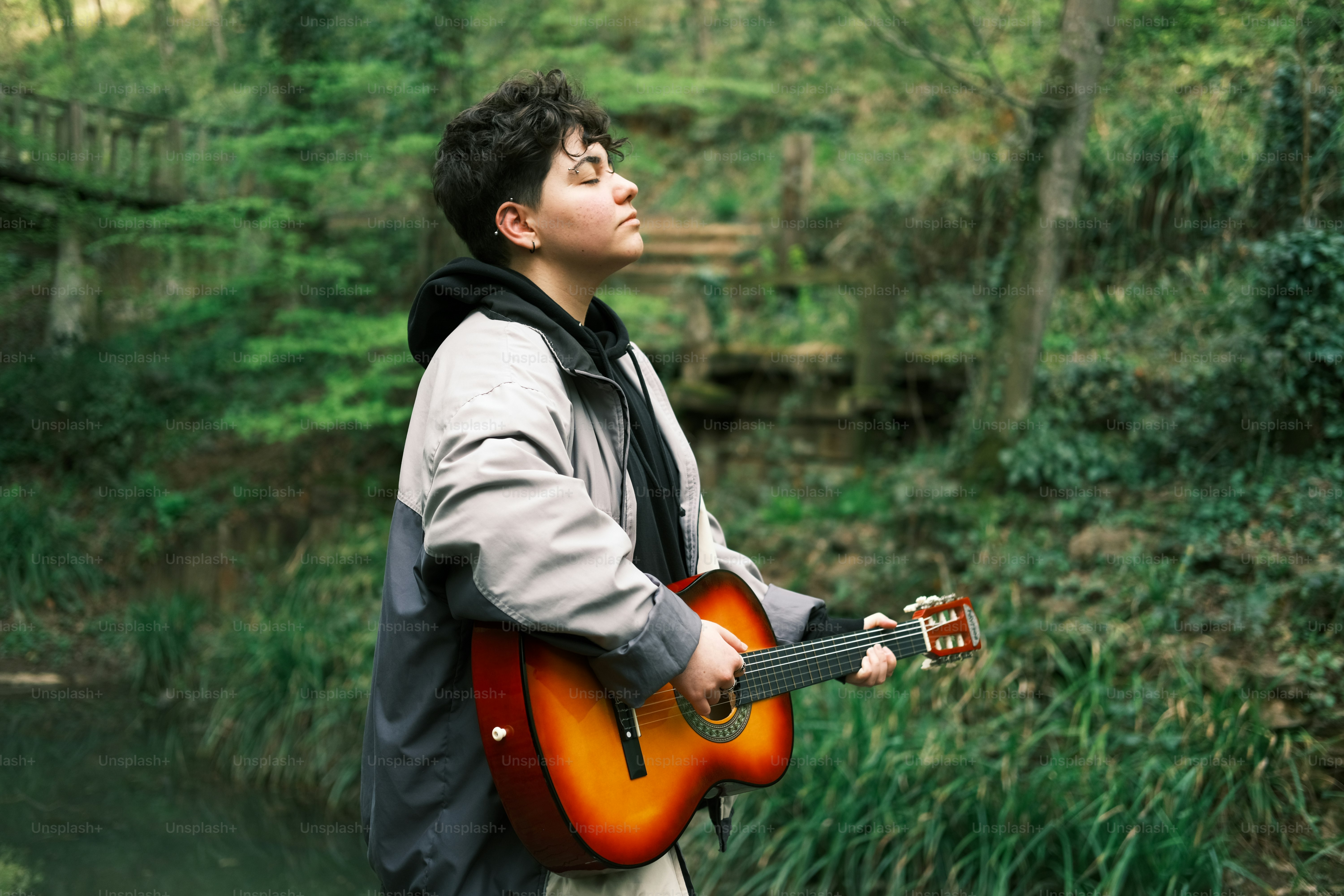 a man holding a guitar standing in front of a river