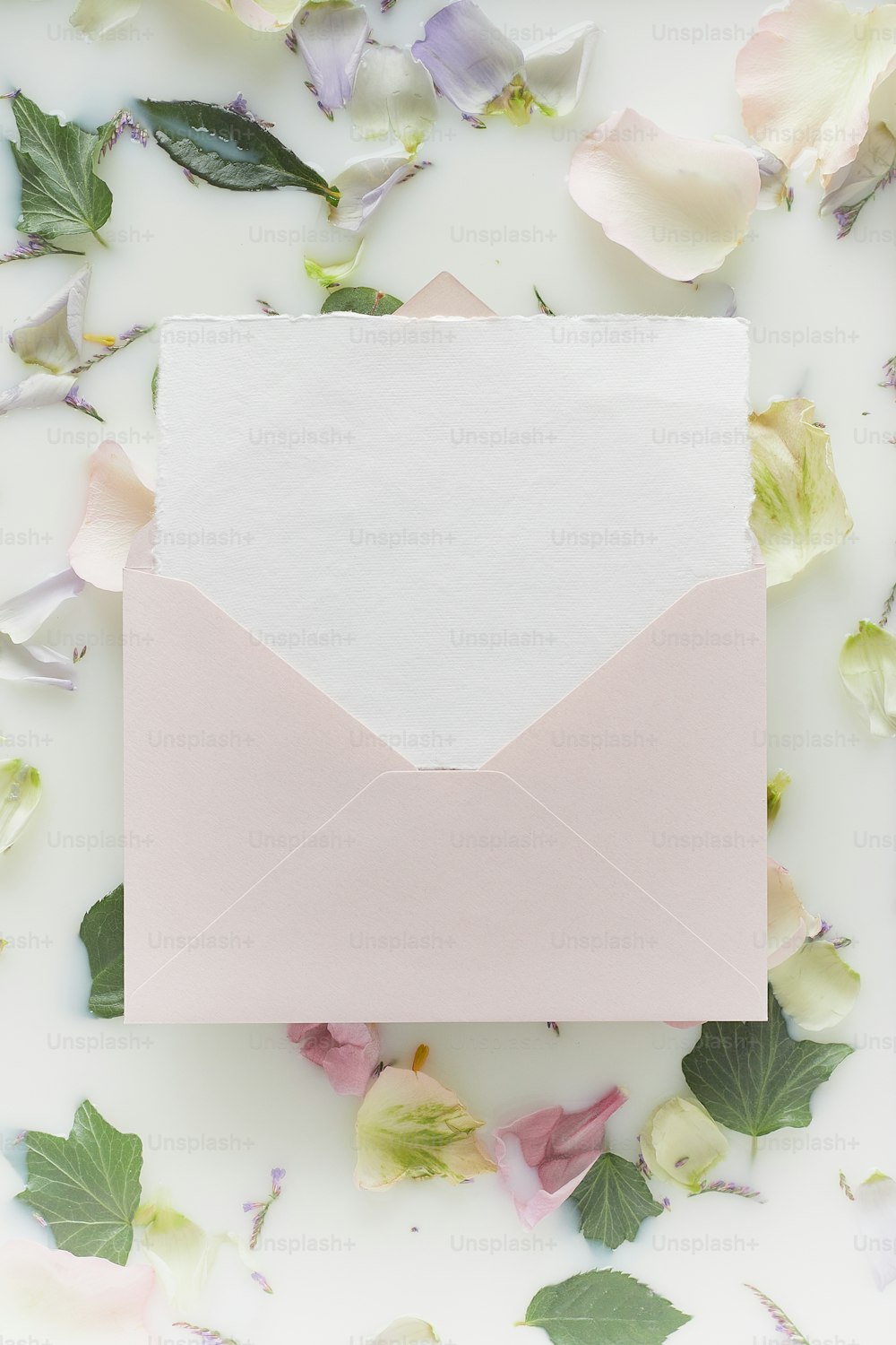 Un sobre blanco con un papel rosa en su interior rodeado de flores