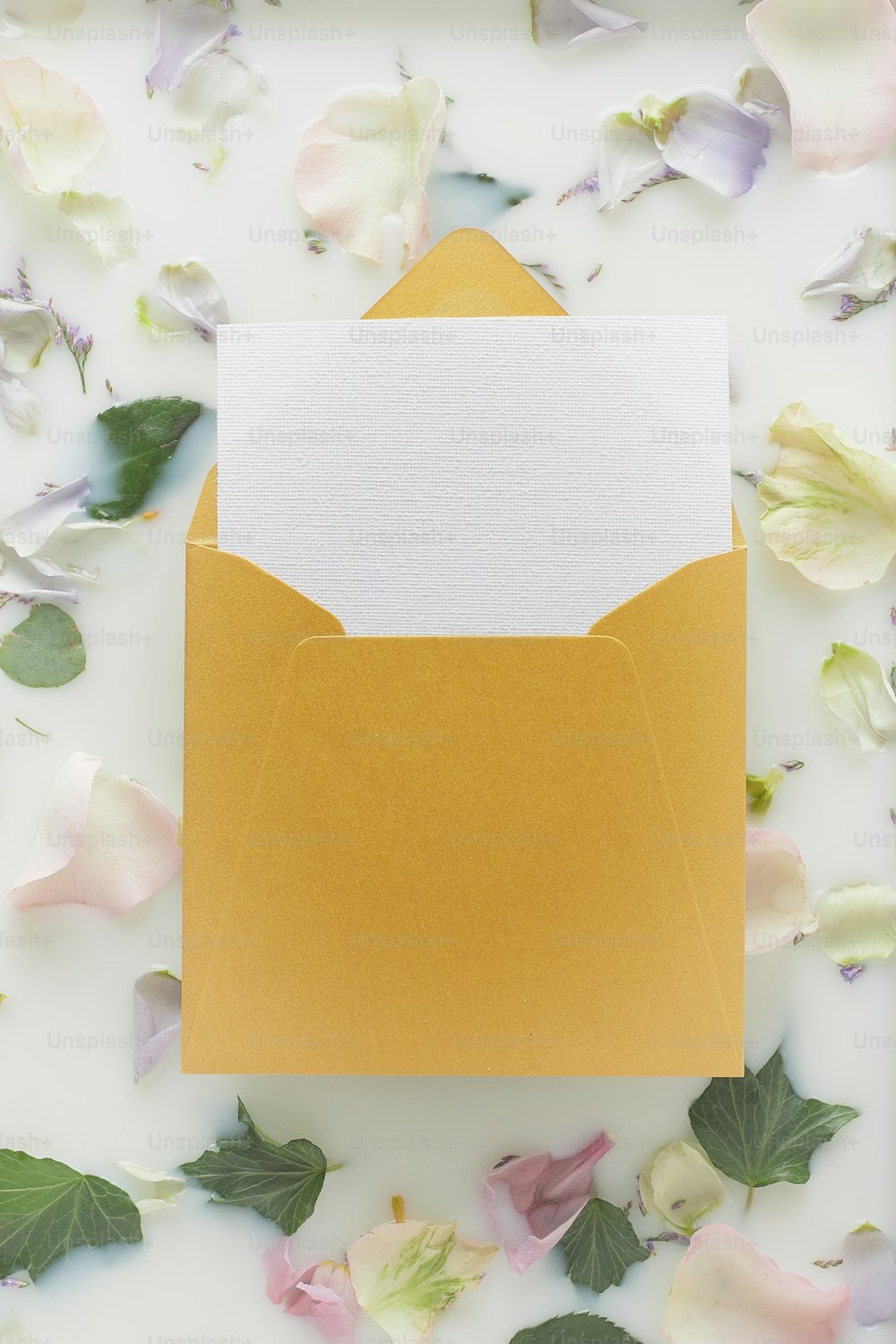 Un sobre amarillo con una tarjeta blanca en el interior rodeada de flores