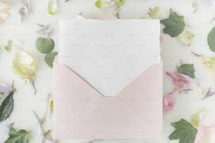 ein rosafarbener Umschlag mit einem weißen Papier im Inneren, umgeben von Blumen
