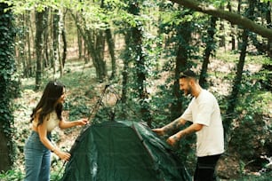 a man and woman setting up a tent in the woods