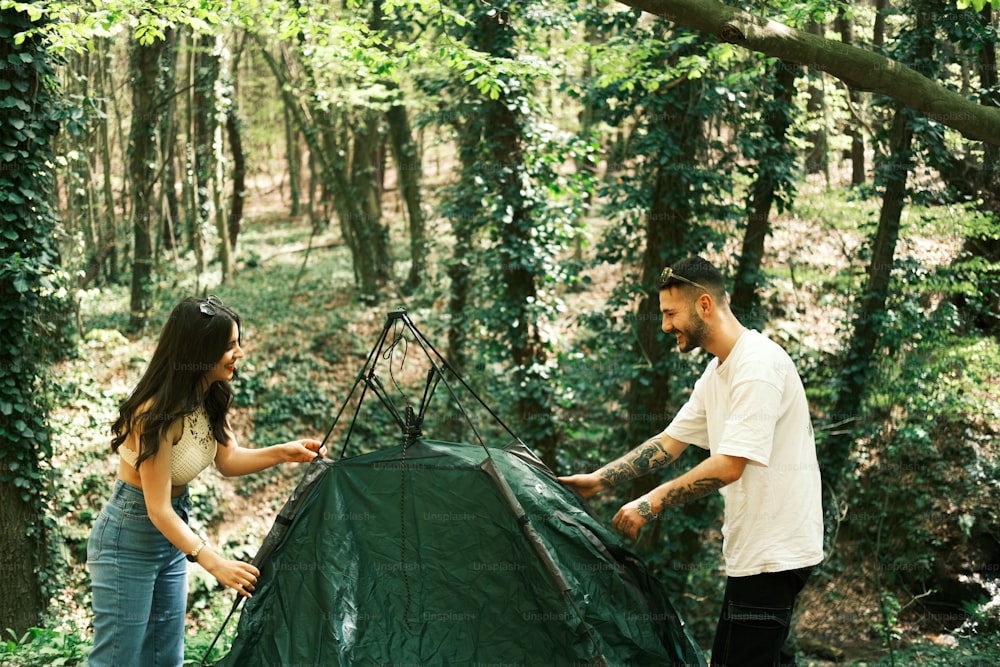 a man and woman setting up a tent in the woods