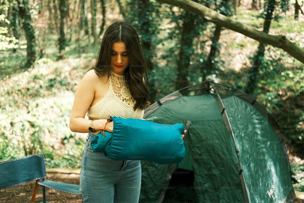 a woman holding a sleeping bag in front of a tent