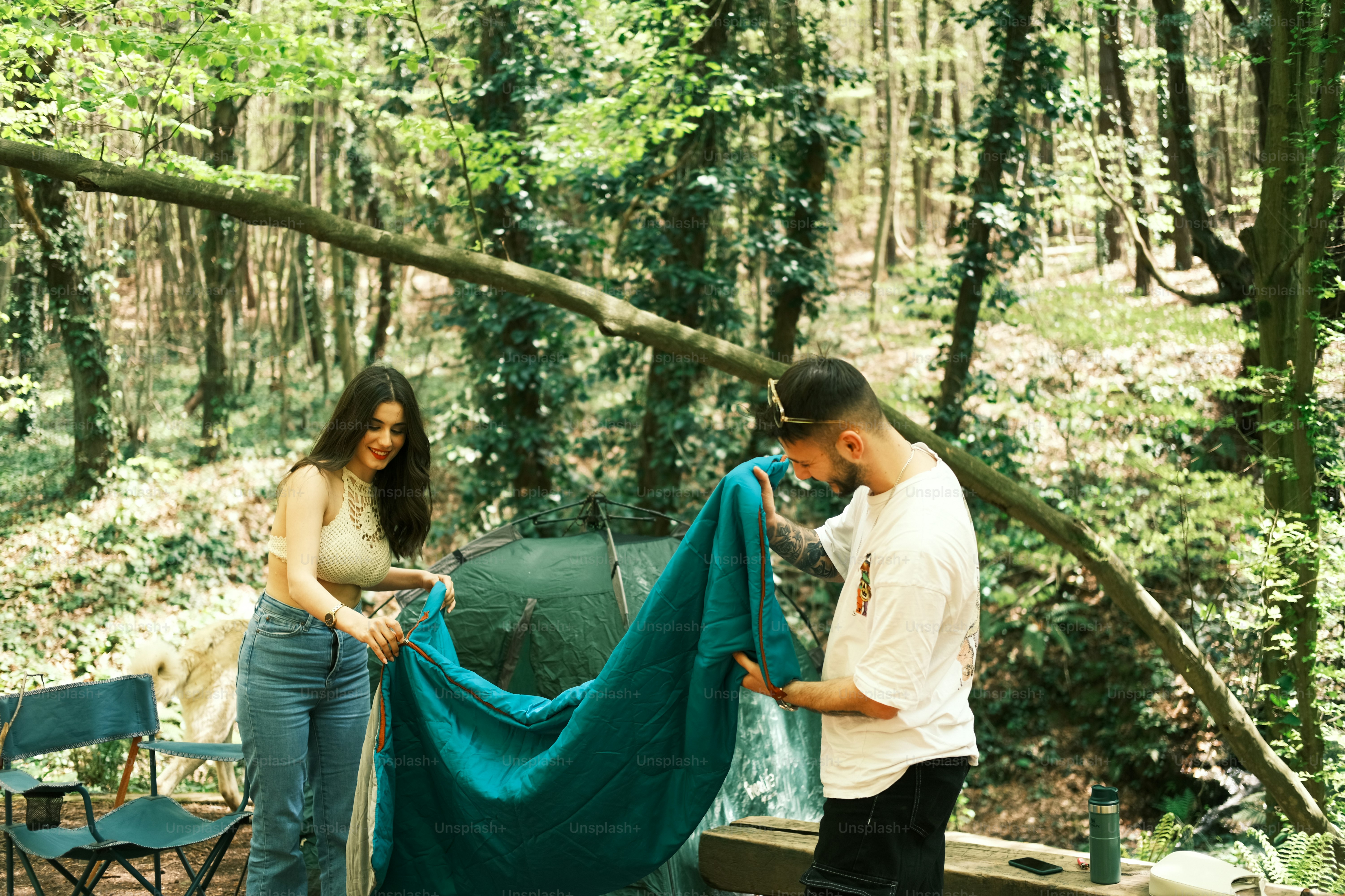a man and a woman standing next to a tent in the woods