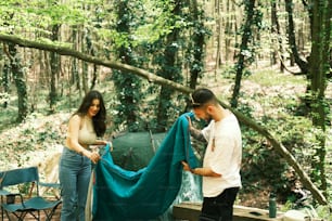 a man and a woman standing next to a tent in the woods