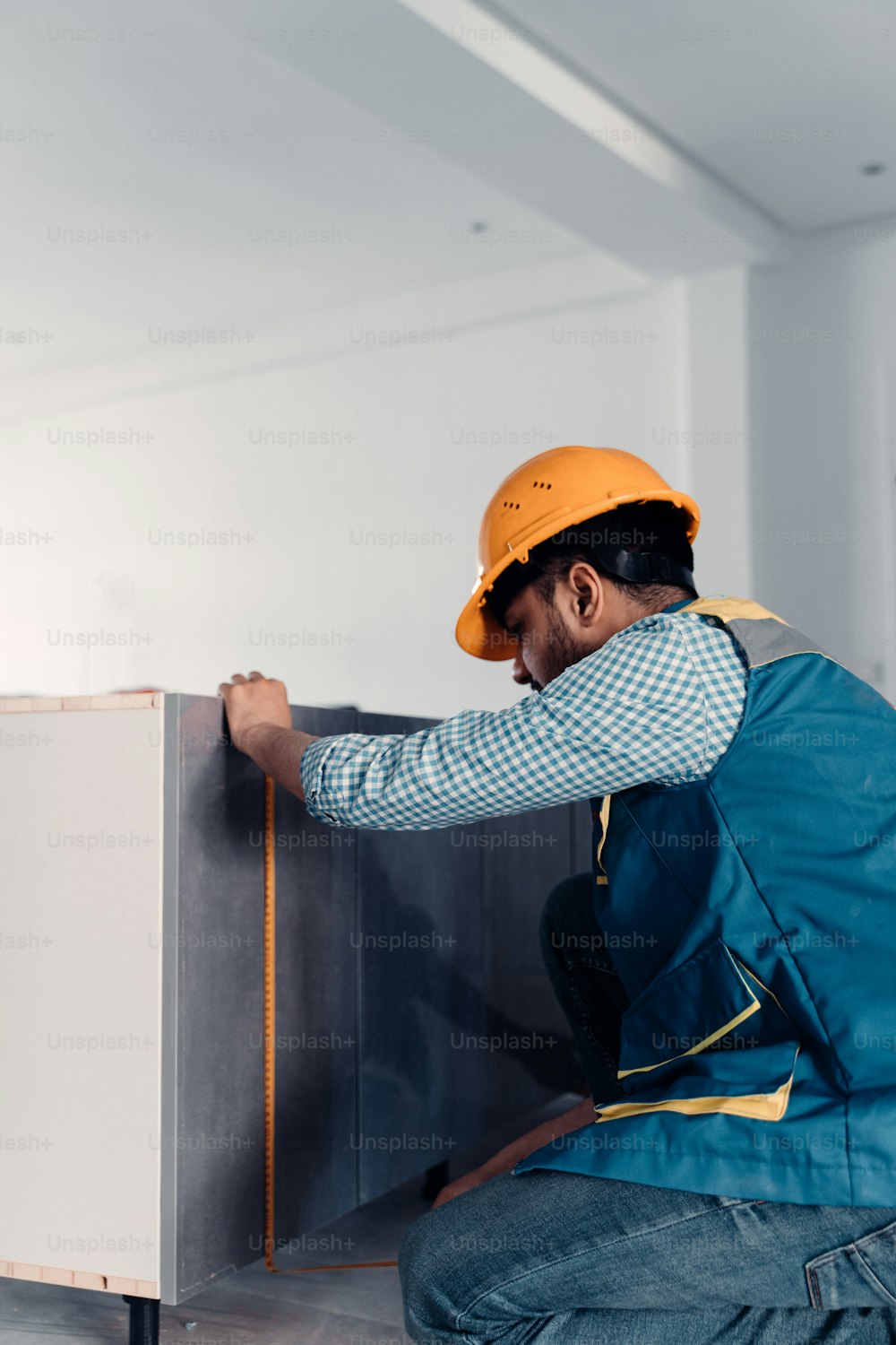 a man in a hard hat and overalls working on a cabinet