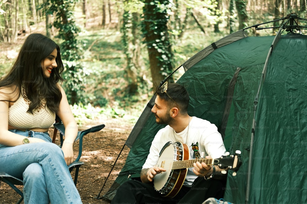 Un hombre tocando una guitarra junto a una mujer sentada en una silla