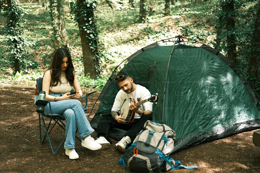 a man and a woman sitting next to a tent in the woods