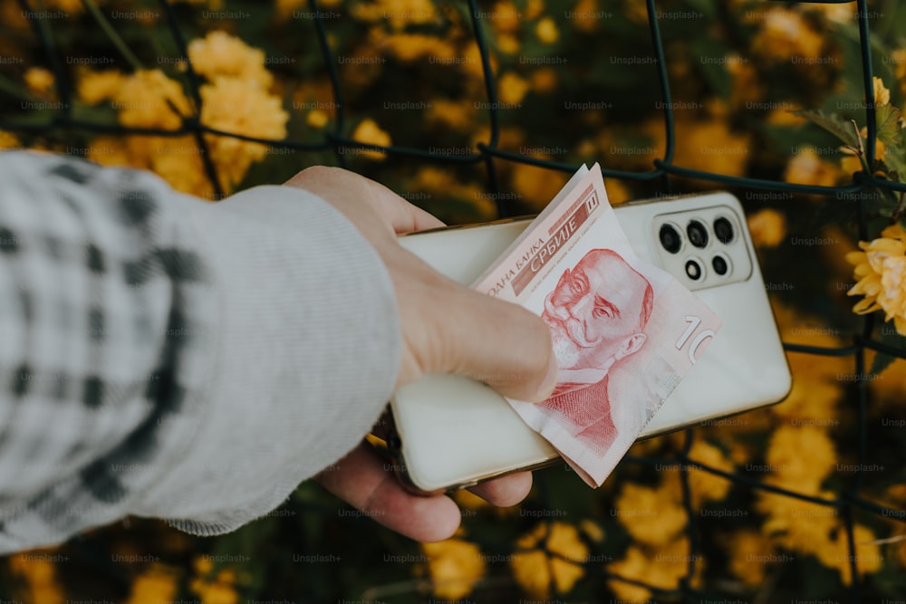 a person holding a money in front of a fence