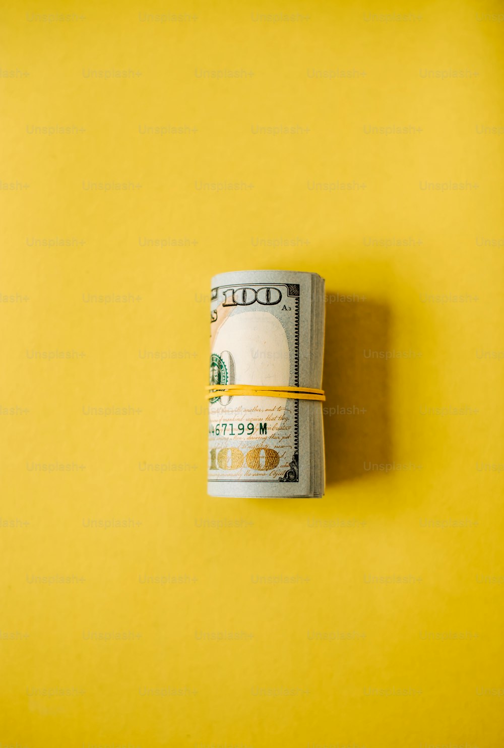 a stack of one hundred dollar bills on a yellow background