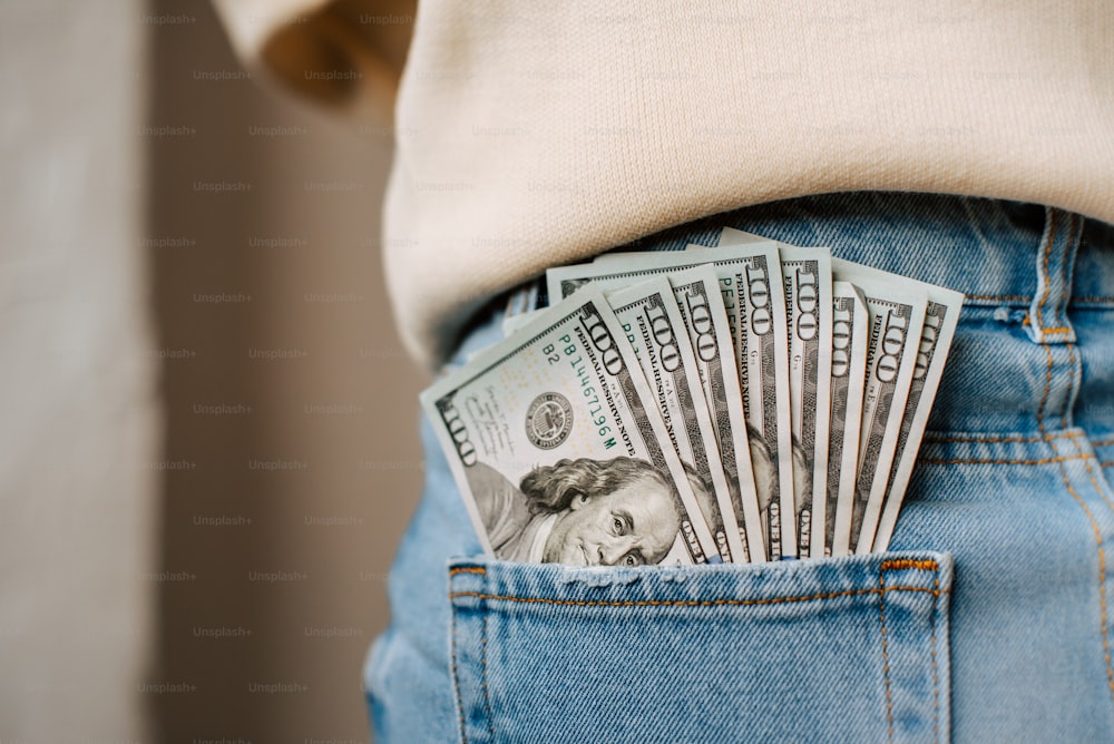 a person is holding a stack of money in their back pocket