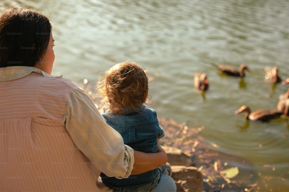 a woman and a child looking at ducks in the water