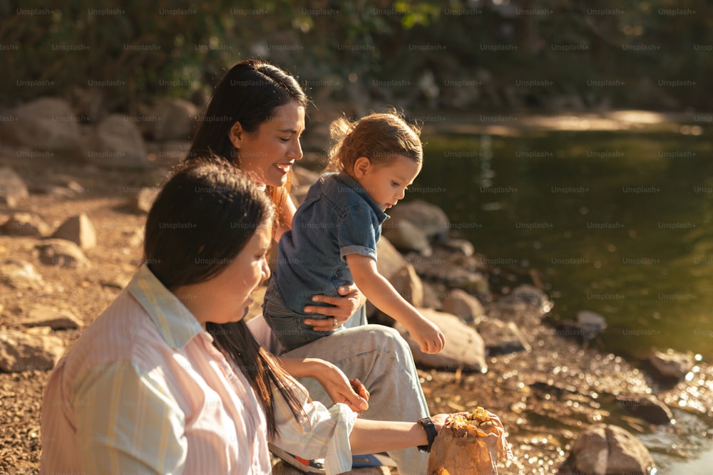 水辺の岩の上に座っている女性と2人の子供