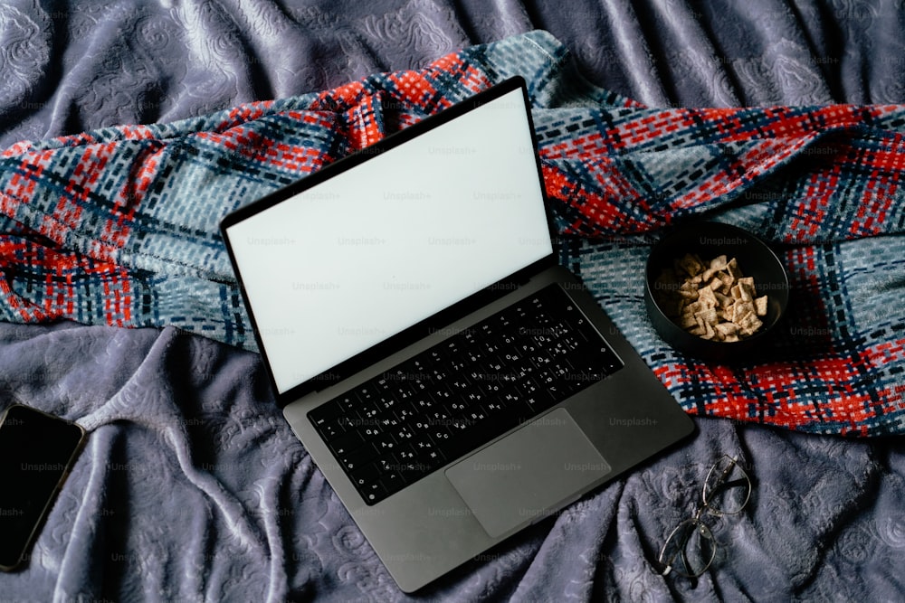 a laptop computer sitting on top of a bed next to a bowl of cereal