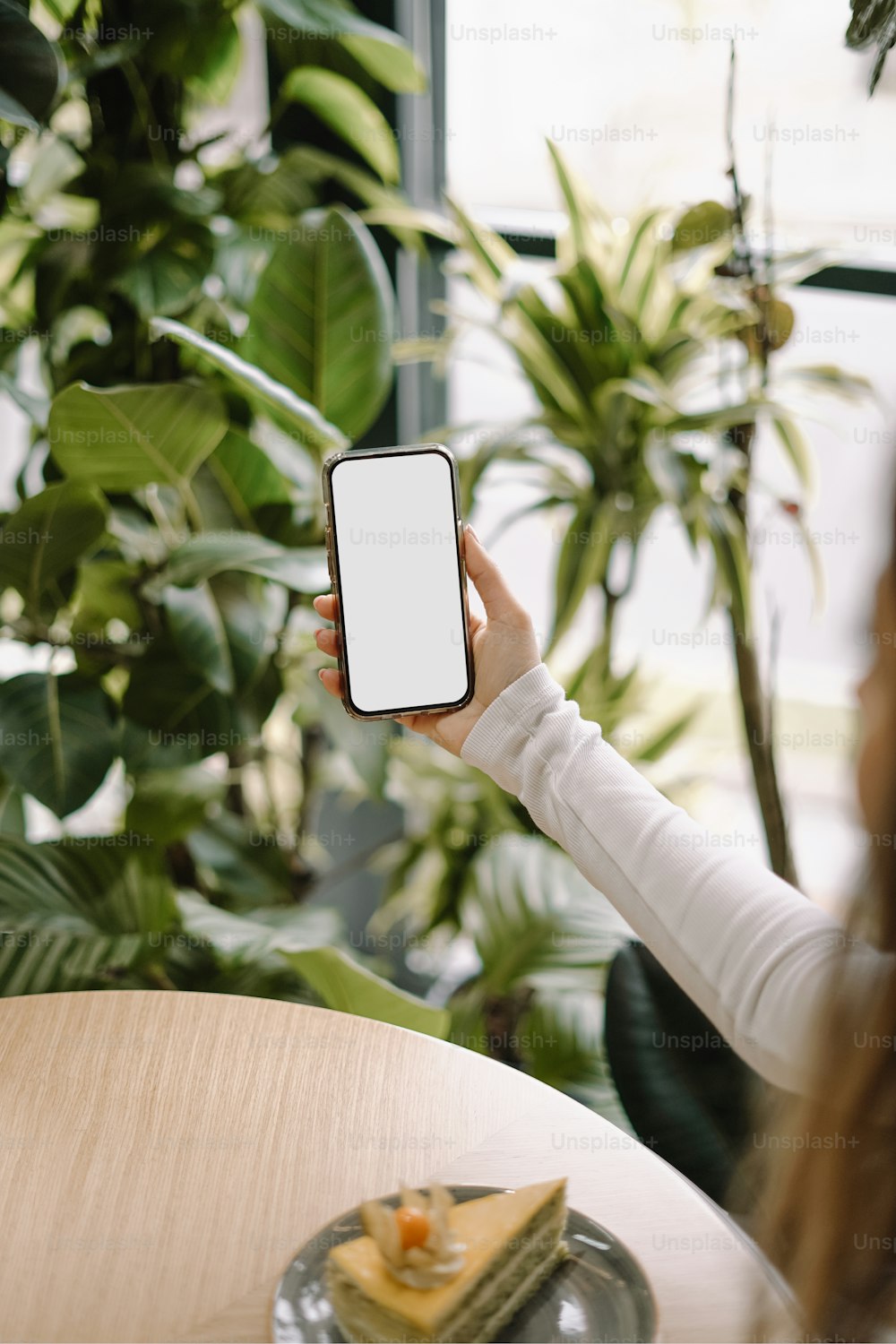 a woman holding up a smart phone in front of a plant