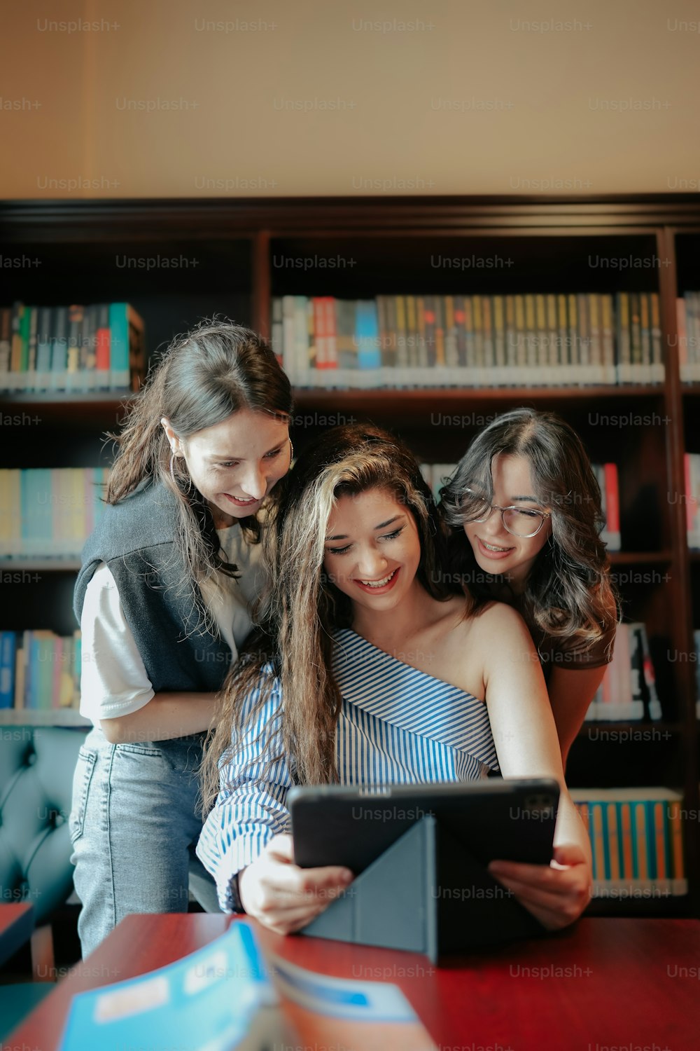 three girls looking at a tablet in a library