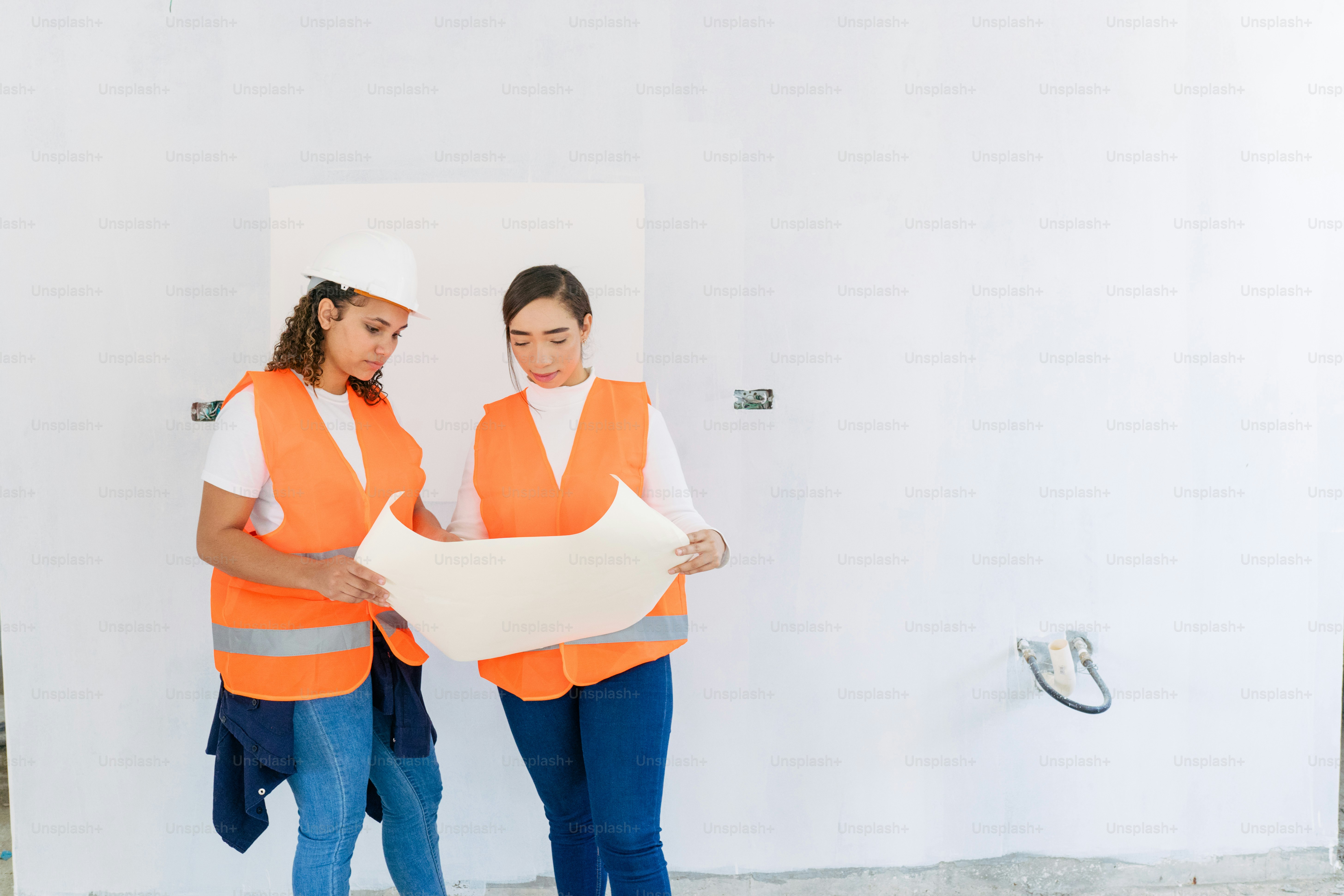Zwei Frauen in orangefarbenen Westen, die ein Stück Papier halten
