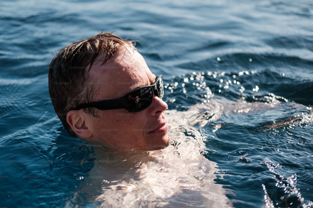 a man swimming in the ocean wearing sunglasses