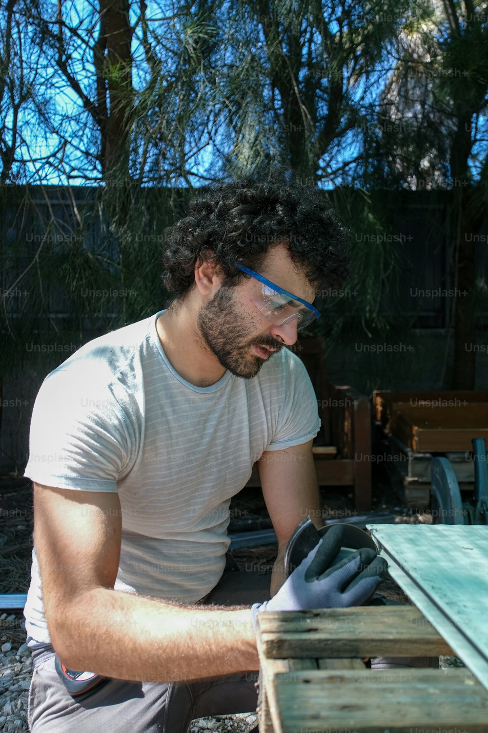 a man in a white shirt and black gloves working on a piece of wood