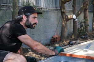 um homem de camisa preta e chapéu trabalhando em um pedaço de madeira