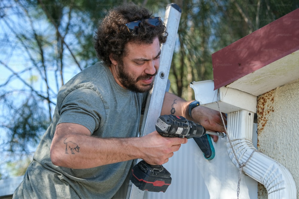 Ein Mann, der einen Bohrer benutzt, um eine Dachrinne zu reparieren