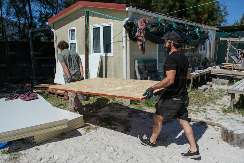 um homem carregando uma mesa de madeira na frente de uma casa