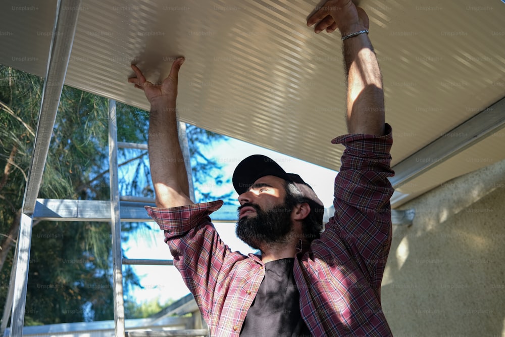 a man with a beard and a plaid shirt is holding up a metal roof