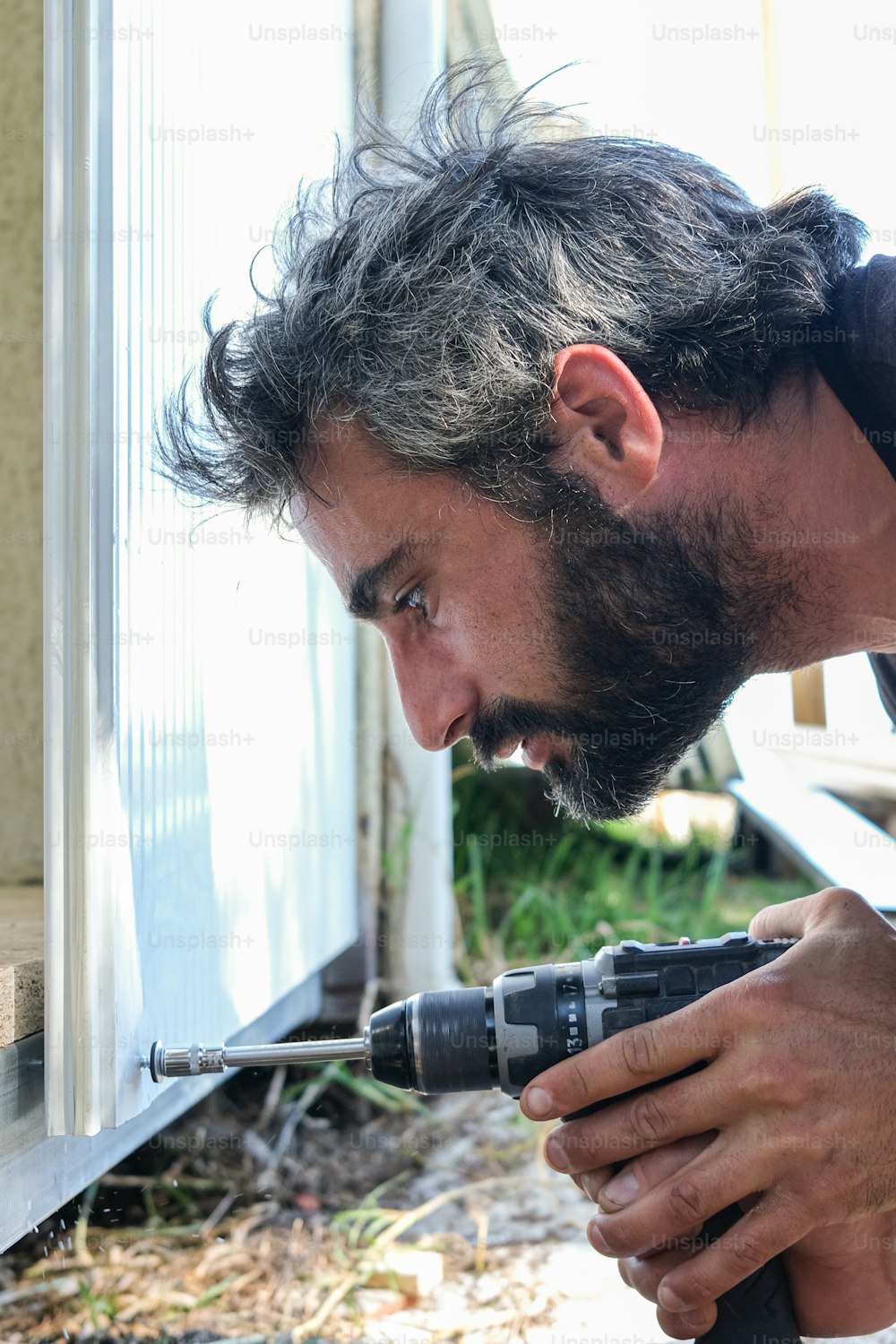 Un hombre usando un taladro para arreglar una ventana