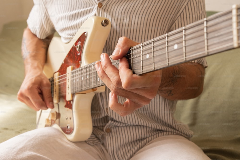 um homem sentado em uma cama tocando uma guitarra